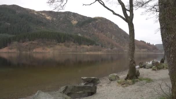 スコットランドの曇りの日に 前景に岩と背景に山がある湖の海岸から撮影された追跡とパンニング — ストック動画