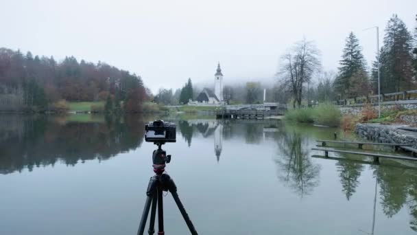 Фотоаппарат Треноге Озере Бохинь Фотографирует Живописную Церковь Потрясающим Отражением Туманных — стоковое видео