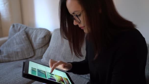 Σοβαρή Νεαρή Γυναίκα Κάθεται Στον Καναπέ Κύλιση Ένα Tablet Που — Αρχείο Βίντεο