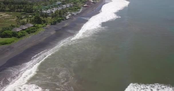 インドネシアのバリ島の海岸線にある黒い砂のビーチと海の波の空中ビュー ドローンショットを傾ける — ストック動画