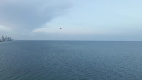 穏やかな青い海を飛んでいる赤い沿岸警備隊のヘリコプターの広いショット — ストック動画