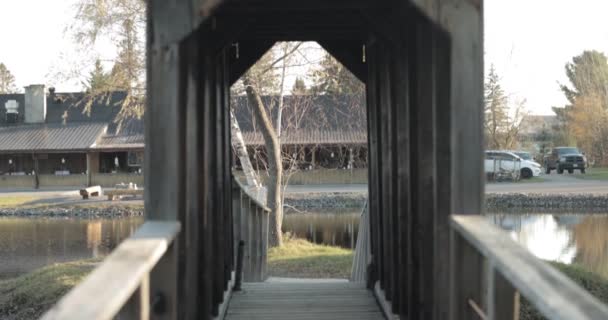 慢动作的手拿着夹子穿过一座木人行天桥 桥穿过池塘 来到一座岛上 后面是一座接待楼 Bean Town Ranch — 图库视频影像