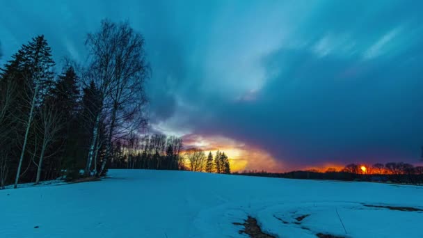 冬の雪原の上にオレンジ色の日の出の照明と朝の夜明けに飛んで劇的な雲 — ストック動画