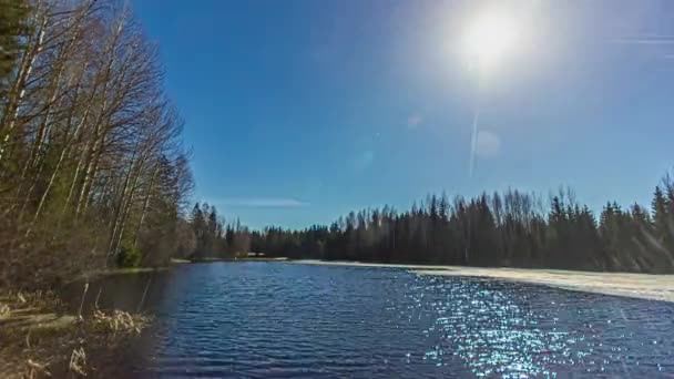 昼間に木々に囲まれて太陽が動くにつれて 凍結した湖が溶けていくのをタイムラプス撮影 春の間に融雪する雪の池と農村風景のタイムラプス — ストック動画