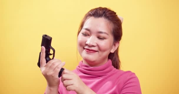 在明亮的黄色背景下 对着手枪检查弹药是否安全的亚洲女人进行近距离微笑 — 图库视频影像