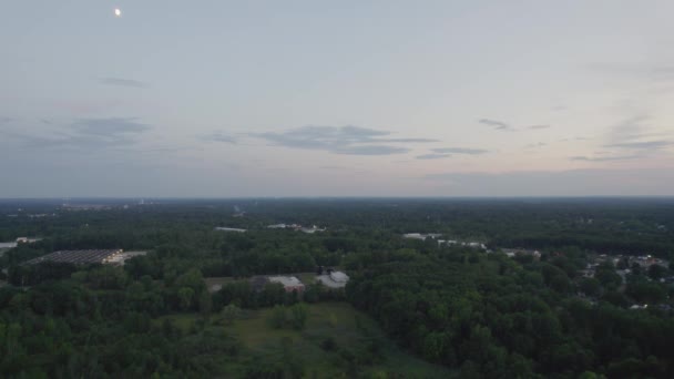 日没後の夕方に緑豊かな植生に囲まれた町の上に空中ドローンショット — ストック動画