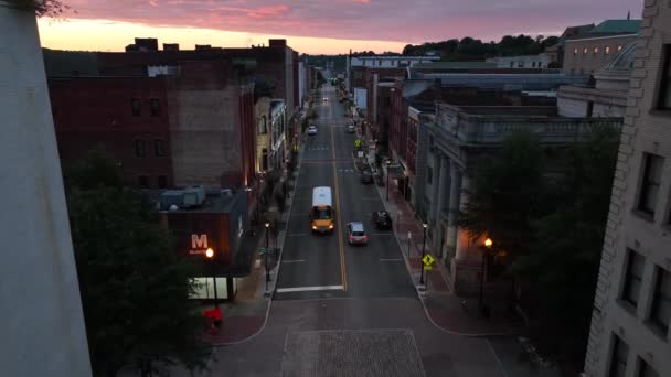 日の出の間にダウンタウンの都市の町を通る黄色のスクールバス 空中追跡射撃 — ストック動画