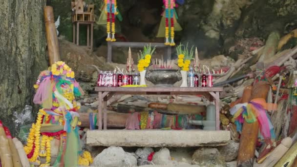 先祖のための飲み物とテーブルの上で煙で燃焼線香 カラフルな花やリボンで飾られた洞窟の中で仏教のタイの祈りの場所 — ストック動画