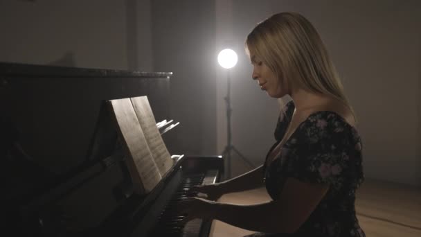 女性ピアニストは新しいピアノ音楽のパートを学びます 単独で彼らの光の背景とスタジオで — ストック動画
