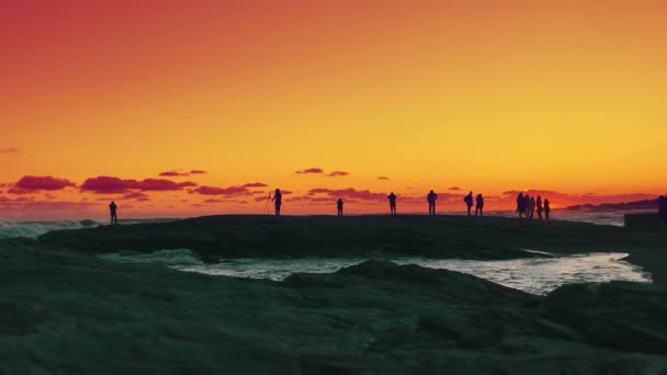 Silhouettes People Beach Enjoying Sunset Waves Splashing Rocky Coast — Stock Video