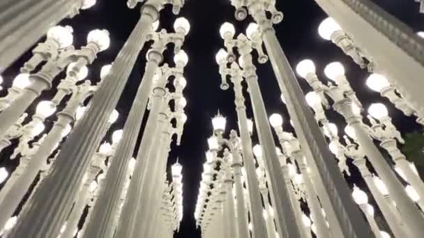 夜を見上げるラッカ都市光の彫刻の真ん中の行を歩く — ストック動画