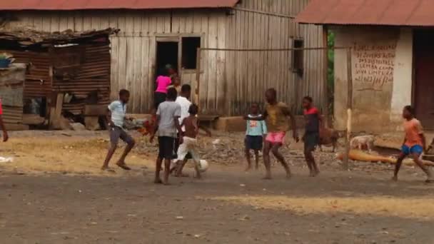 在非洲一个贫穷的村庄的破烂不堪的房屋前踢足球的孩子们 枪林弹雨 — 图库视频影像