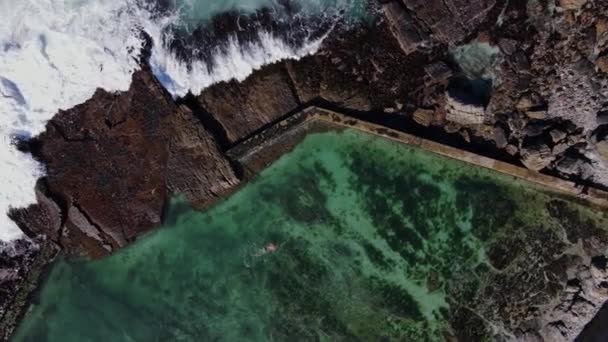 墜落する波と岩の多い海岸の潮溜まりで泳ぐ人間の空中トップダウン — ストック動画