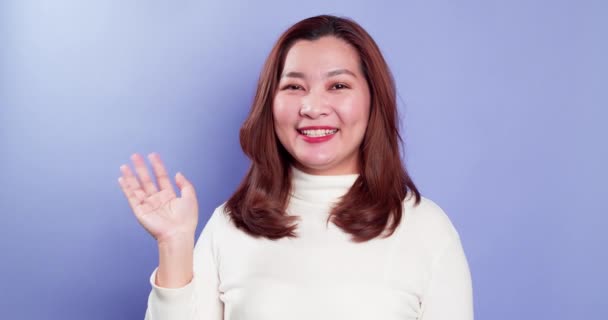 アジアの幸せな女性の肖像画は カメラに手を振っているとバイオレットの背景に隔離されたままハロージェスチャーを行う — ストック動画