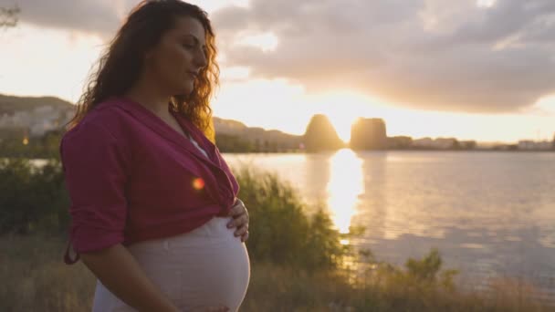 Έγκυος Μαμά Βαθιά Στη Σκέψη Στο Ηλιοβασίλεμα Χαμογελώντας Και Χαϊδεύοντας — Αρχείο Βίντεο