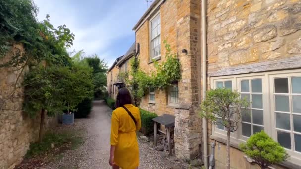 ブロードウェイの典型的なコッツウォルズの家の間を歩く美しい少女の眺め イギリス イギリス — ストック動画