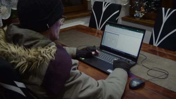 その男は加熱されていない部屋のノートパソコンで働いている 彼女は寒さから身を守るために冬服を着て — ストック動画