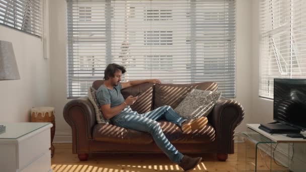 男はソファに横になって電話でスクロールします 快適な家のインテリア — ストック動画