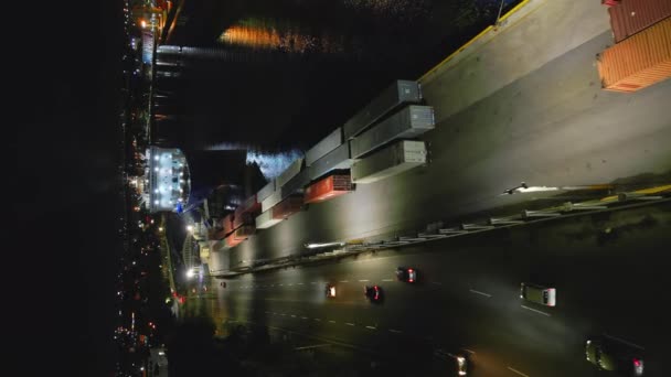 暗い夜の間にサントドミンゴの船とコンテナ港で道路上の車の上の空中垂直飛行 川の岸のコンテナ駐車場 — ストック動画