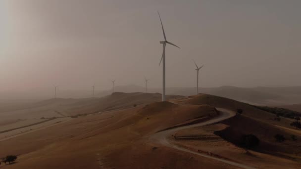 在雾蒙蒙的天气里 在日落或日出时分 追踪一条蜿蜒曲折的道路 通往几个风力涡轮机的航拍 — 图库视频影像