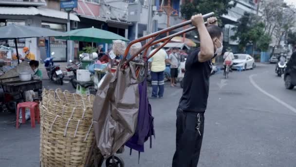 在泰国曼谷 蒙面的男工穿过街道 用空的大篮子把手推车拖在后面 向右转 跟踪射击 — 图库视频影像