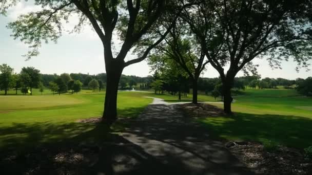 カントリークラブのゴルフ場で木に囲まれたカートの道を歩くと — ストック動画