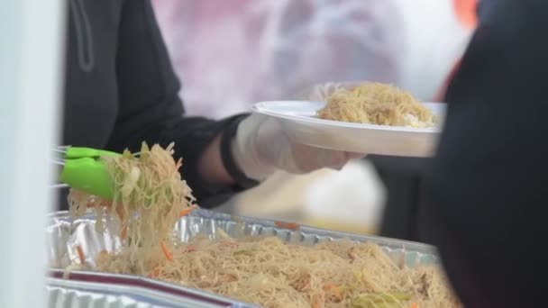 白いプラスチックプレートにトング 屋外ビュッフェで新鮮な熱々の麺を提供する人 — ストック動画