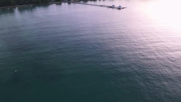 緑の山で日の出の間に桟橋に熱帯青の水の上にドローンの空中パン — ストック動画