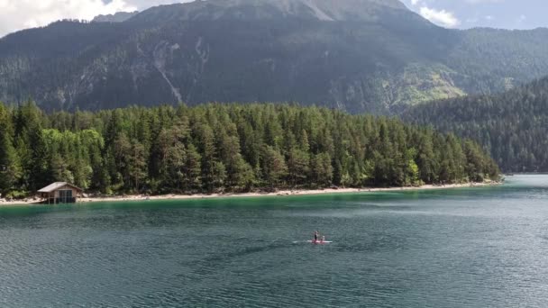 人が立ち上がるオーストリアの山の中のブラインド湖のパドルボードチロル 背景の湖のそばの小屋 — ストック動画