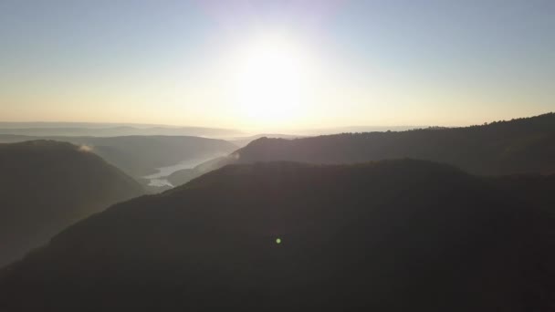 日の出時にタルニタ湖周辺の丘や風景の空中ビュー 明るい太陽の地平線と地形上の朝の霧と低雲 左パン — ストック動画