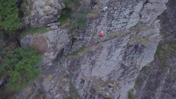 背の高い岩の崖の顔をスケーリング山の登山家の無人機からの空中ビューを上昇 ドローンバックは高い山の上の登山者の広いビューを提供します — ストック動画