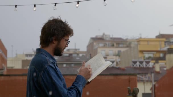 Blanke Man Leest Een Boek Onder Regen Met Gebouwen Achtergrond — Stockvideo