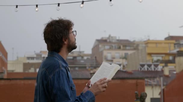 本を持っている男 読書を停止し 雨の日に空を見上げます — ストック動画