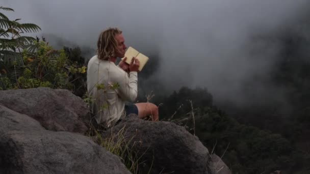 Homem Artista Sentado Rocha Topo Uma Montanha Nebulosa Fecha Seu — Vídeo de Stock