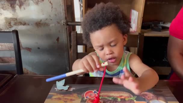 彼の食事を待っている間 テーブルの中で釣りゲームで遊んでいる素敵なエキゾチックな2歳の子供 — ストック動画