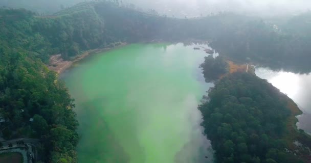 晴れた日の霧の中でTelaga Warna湖の軌道ドローンショット Dieng高原観光アイコンの 中央ジャワ インドネシア 湖の水の色は緑です 湖と森の静かな映像 — ストック動画