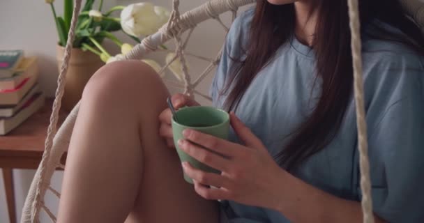 一位年轻的女士手拿着杯子 坐在摇椅上在家里休息 — 图库视频影像