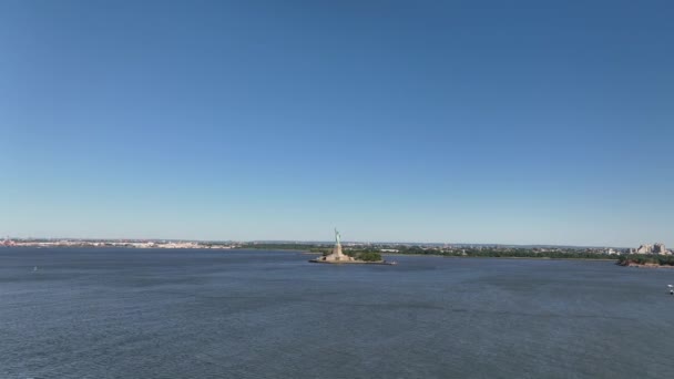 阳光明媚 蓝天晴朗的纽约港口鸟瞰图 当渡船从右边驶入视野时 无人驾驶相机在足够高的地方俯瞰自由女神像的背影 — 图库视频影像