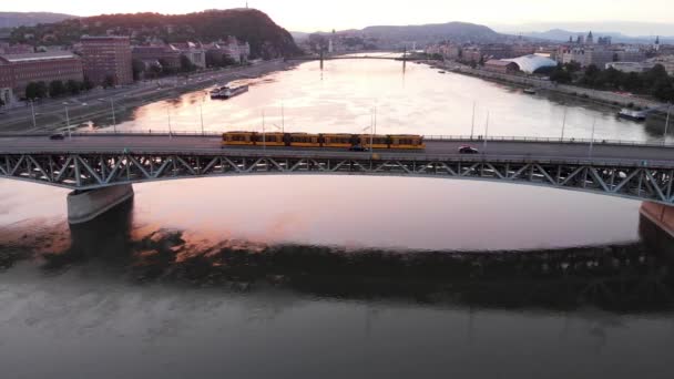 ブダペストの黄色いトラムに続き ドナウ川の美しい夕日のペトフィ橋 — ストック動画