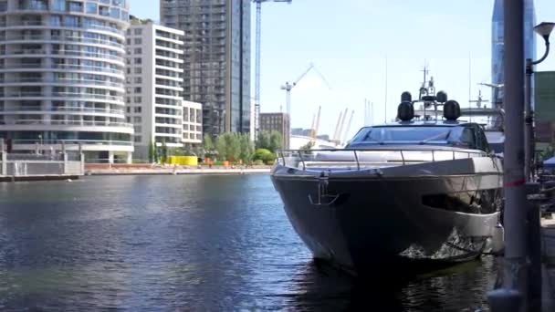 大規模な豪華なボートは 背景に近代的なアパートの建物と晴れた夏の朝の間にロンドンのカナリーワーフの運河の側面にドッキングされています — ストック動画