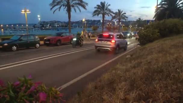 黄昏时分 人们在棕榈树和路灯之间的人行道上漫步 车流流畅 城市的海港在暮色的背景下 全景镜头被挡住了西班牙Pontevedra Porto Novo — 图库视频影像