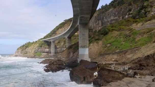 Onde Bianche Che Infrangono Sulle Rocce Sotto Grande Ponte Curvo — Video Stock