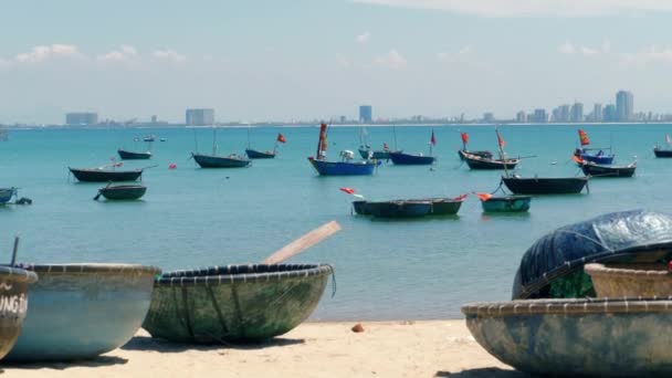 海岸線の近くに停泊している通常のボートと一緒に晴れた日の午後に海岸沿いに休んでいる丸いベトナムの漁船の静止したクローズアップ映像 — ストック動画