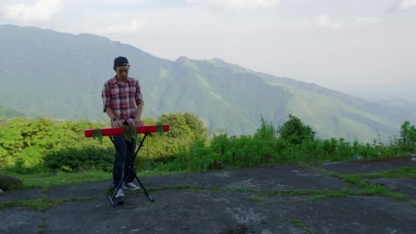 3分の1の法則の左側の線から男の静止した映像 背景に山の景色と彼の電子音楽キーボードを再生 彼はキーボードに接続されているペダルも使用します — ストック動画