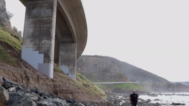 Άνθρωπος Περπατά Προς Την Κάμερα Κάτω Από Γέφυρα Sea Cliff — Αρχείο Βίντεο