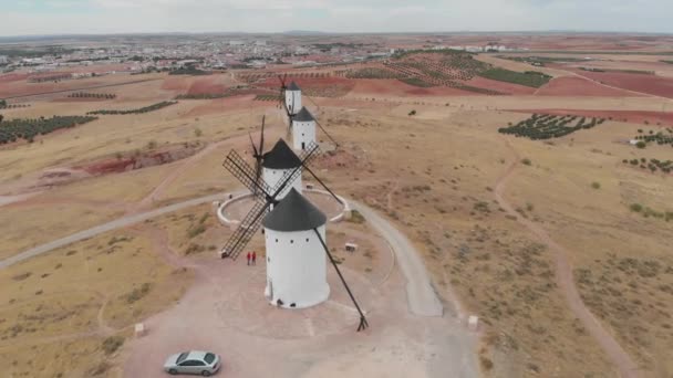 背景の人々が交流し 土地やプランテーションとして丘の上に置かれた白い風車の上を飛行する空中のドリーショット — ストック動画