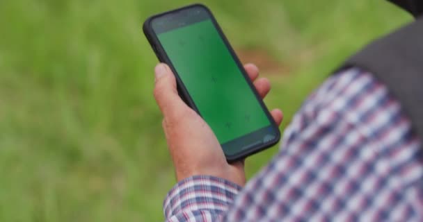 牛仔带着绿色屏风带着智能手机在农场边走来走去 手持慢动作 — 图库视频影像
