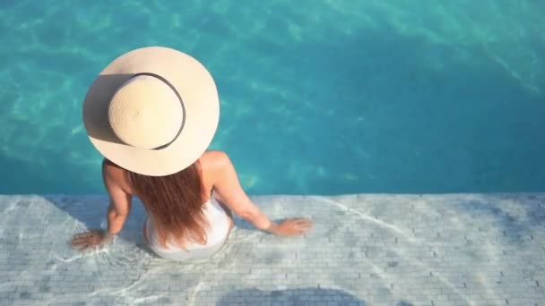回到摄像机前 一个戴着大草帽的女人坐在游泳池的台阶上 — 图库视频影像
