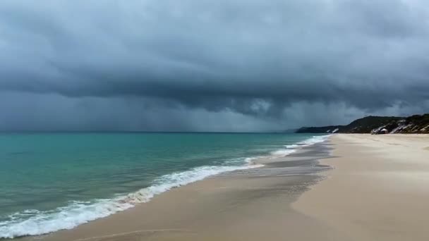 層とコントラスト 穏やかなラップ波は 緑の太平洋の上に雨を降らす暗く怒っている嵐のシャワーとして平和的なビーチに洗い流されます — ストック動画