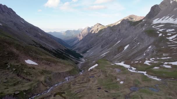 氷河の谷に面した空中無人偵察機の映像は スイスの雪と高山草原の残りのパッチと劇的でギザギザの山の風景をゆっくりと反転させます — ストック動画
